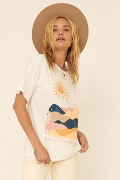 Distressed graphic t-shirt. Vintage-style landscape art print with "Live in the Moment" text. Slashed and distressed detailing at neckline, cuffs, and hem. Round neckline. Short sleeves. Drop shoulder. Relaxed fit. 100% Cotton. Imported top designed and printed in LA. Model wears size S. Cream Graphic Print Top For Summer, Cream Tops With Screen Print For Spring, Cream Graphic Print Top For Spring, Spring Cream Top With Screen Print, Free-spirited Cotton T-shirt For Summer, Summer Cream Graphic Tee T-shirt, Cream Graphic Tee For Summer, Free-spirited Graphic Print Short Sleeve T-shirt, Artsy Summer Tops With Letter Print