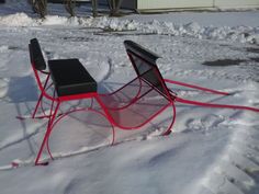 a red sled sitting in the snow next to a black table with a laptop on it