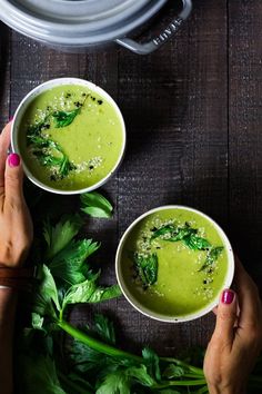 two hands holding bowls of green soup with parsley