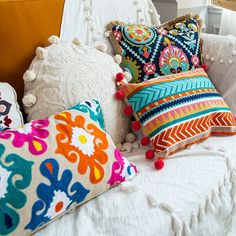 colorful pillows on a white bed with pom - poms and tassels