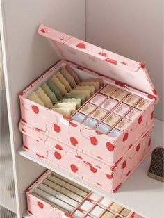 an open pink box filled with lots of different types of cookies on top of a white shelf