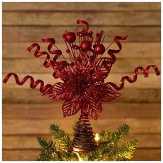 a christmas tree decorated with red ribbon and ornaments on it's top, in front of a wooden wall