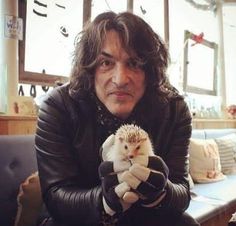 a man sitting on a couch holding a hedgehog in his hands and looking at the camera