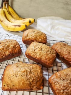 banana muffins cooling on a wire rack next to a bunch of ripe bananas