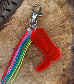 a red boot keychain hanging from a tree stump with a rainbow cord attached to it