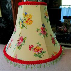 a lamp shade with flowers and red trim hanging from the ceiling in a living room