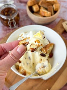 a hand holding a piece of bread over a bowl of ice cream