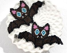 two black cats on a white plate with pink and blue beads in the shape of bats