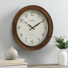 a wooden clock on the wall next to a vase with flowers and an open book