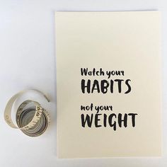 a card with the words watch your habitts not your weight on it next to a roll of money