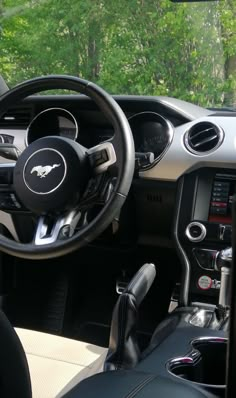 the interior of a car with steering wheel, dashboard and dash board in front of trees