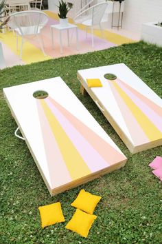 two cornhole boards on the grass with yellow and pink squares around them, sitting next to each other