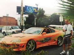 a man standing next to an orange sports car with flames painted on the front and side