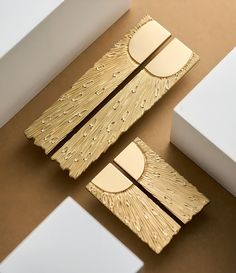 two pieces of gold jewelry sitting on top of a brown table next to white boxes