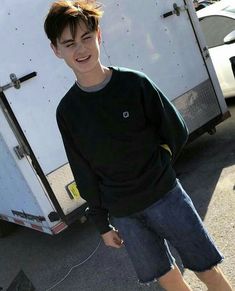 a young man standing in front of a trailer with his hands in his pockets and smiling at the camera