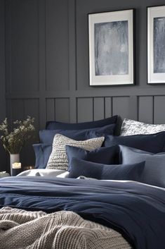 a bed with blue comforters and pillows in a dark room next to two framed pictures on the wall