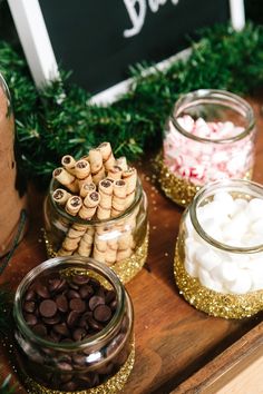 a wooden table topped with jars filled with candy and marshmallows on top of it