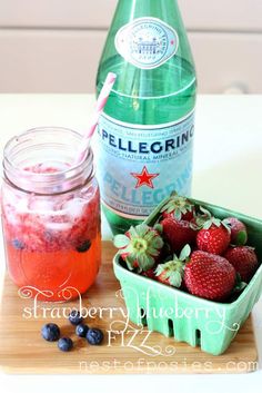 a bottle of water and some strawberries in a container on a cutting board with blueberries