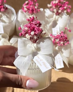 a person holding a small glass jar with flowers in it and tags on the top