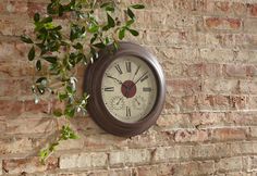 a clock mounted to the side of a brick wall next to a green leafy plant