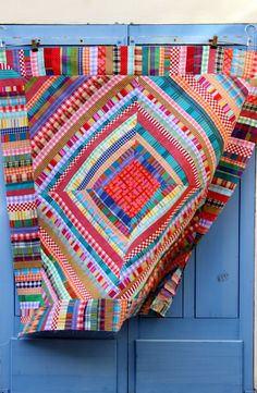 a colorful quilt hanging on the side of a blue door