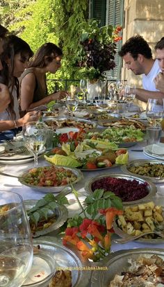 many people are sitting at a long table full of food and wine glasses in front of them