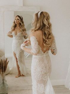 a woman standing in front of a mirror wearing a white wedding dress with long sleeves