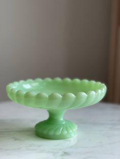 a green cake plate sitting on top of a white marble table next to a window