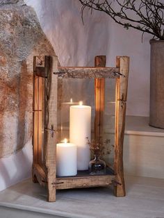 two white candles sitting in a wooden lantern