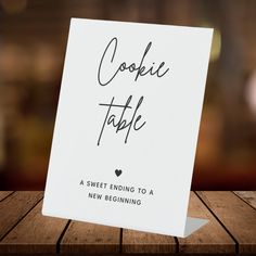 a card with the words cookie table written in cursive ink on it sitting on a wooden surface