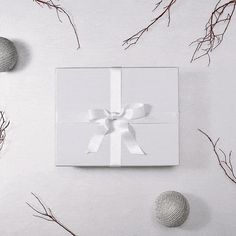 an open white gift box with a white bow on it surrounded by branches and balls