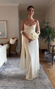 a woman in a white dress is standing on a blue rug and holding a bouquet