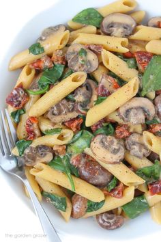 a pasta dish with mushrooms, spinach and sun dried tomatoes in a white bowl