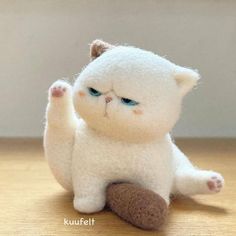 a small white cat sitting on top of a wooden floor next to a wall with its paw in the air