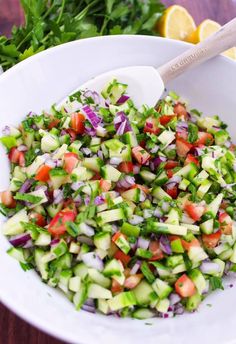 a white bowl filled with cucumber and red onion salad next to lemon wedges