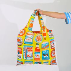 a person holding up a yellow bag with different types of beer on it and logos