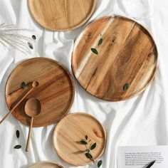 three wooden plates and two spoons on top of a white sheet with green leaves