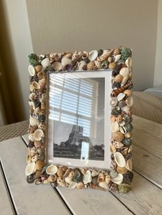 a frame made out of seashells on a wooden table with a window in the background