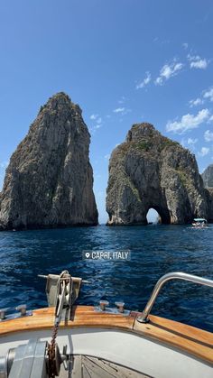 two large rocks in the middle of the ocean next to a boat with people on it