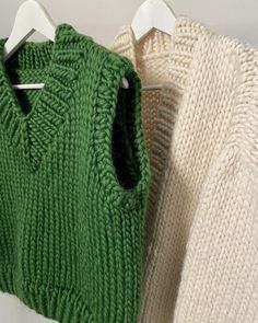 two sweaters hanging on clothes pins next to each other, one green and the other white