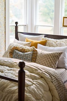 a bed with lots of pillows on top of it next to a window in a bedroom