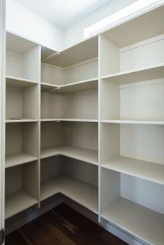 an empty closet with white shelves and wood flooring