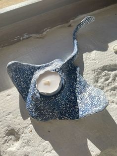 a blue and white flowered hat with a lit candle in it sitting on the sand