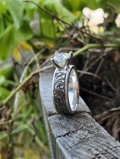 two wedding rings sitting on top of a wooden bench in front of some leaves and branches