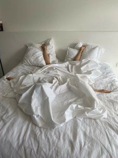 a person laying in bed with white sheets and pillows