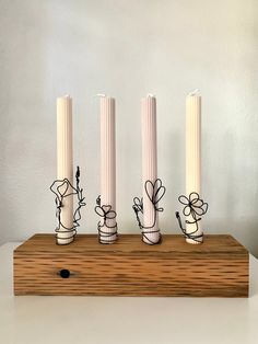 three white candles with flowers on them sitting in front of two smaller ones that are standing upright