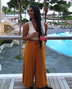 a woman standing on top of a balcony next to a swimming pool and palm trees