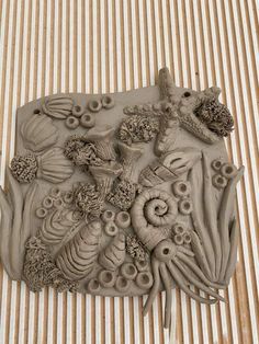 an intricately designed clay sculpture on a striped surface with shells and seaweeds