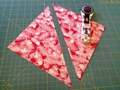 two pieces of red fabric are next to a pair of scissors on a cutting board