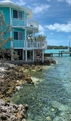 a house sitting on top of a rocky shore next to the ocean with clear blue water